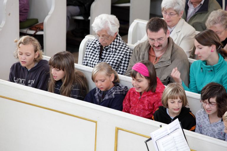 Gottesdienstbesucher sitzen auf weißen Kirchenbänken