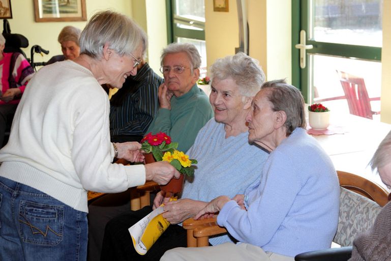 Eine Seniorin verteilt Blümchen an andere Senioren 