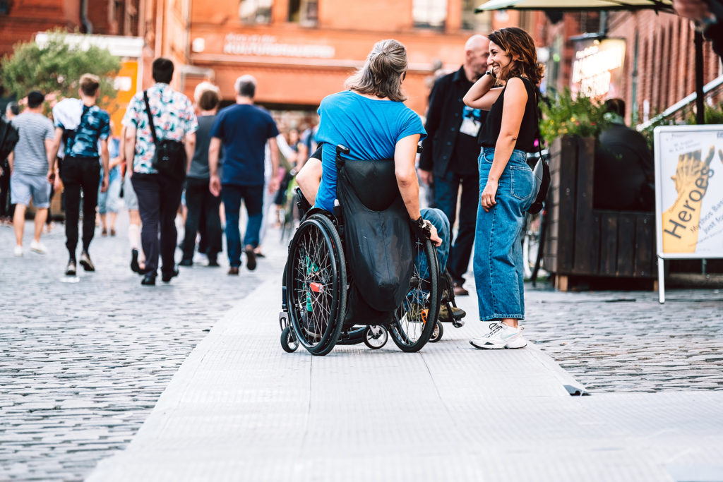 Frau im Rollstuhl unterhält sich bei einer Veranstaltung auf einem Weg, (c) Andi Weiland